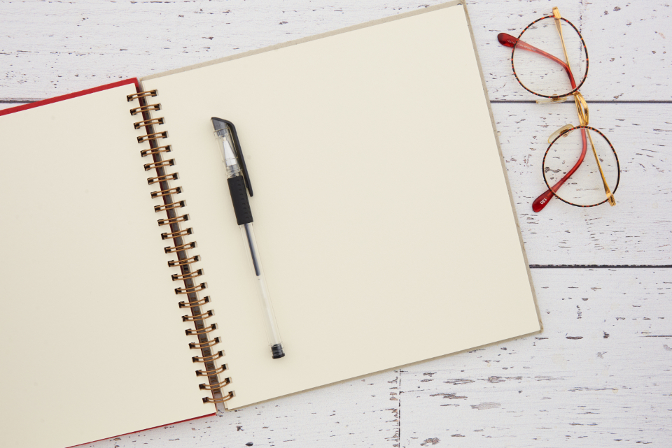 Open notebook, pen and reading glasses on a white desk